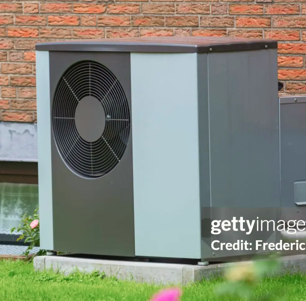 Outdoor heatpump against a brick wall of a house.