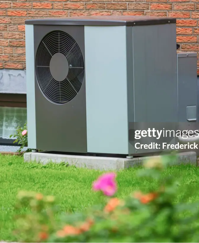 Outdoor heatpump against a brick wall of a house.