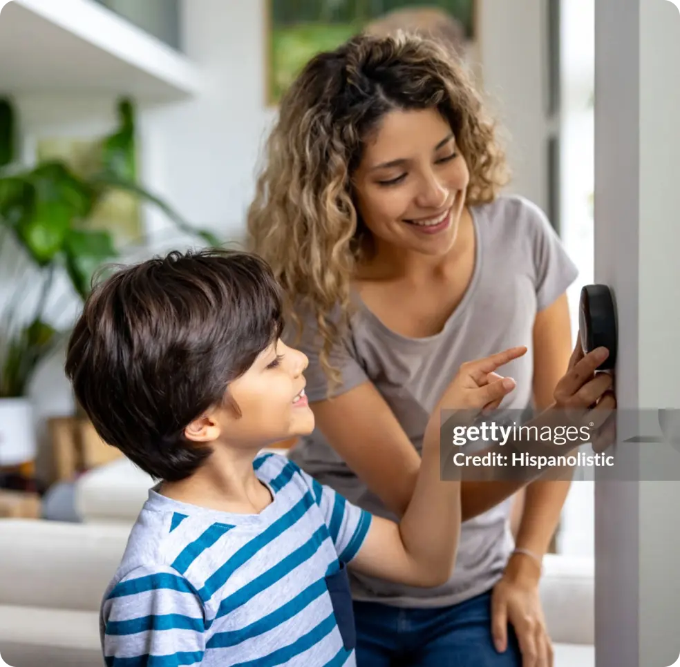 Woman and child adjust thermostat on the wall.