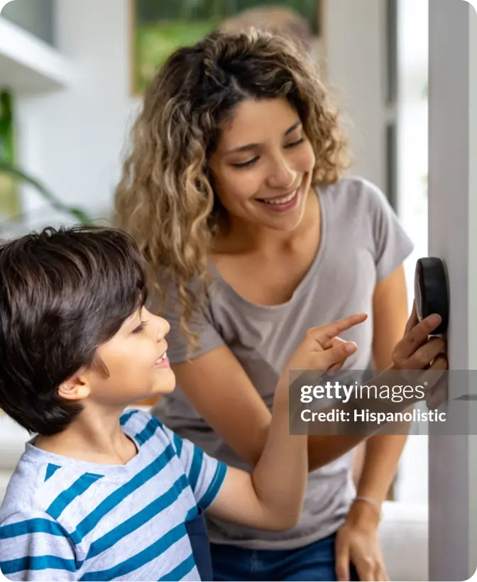 Woman and child adjust thermostat on the wall.