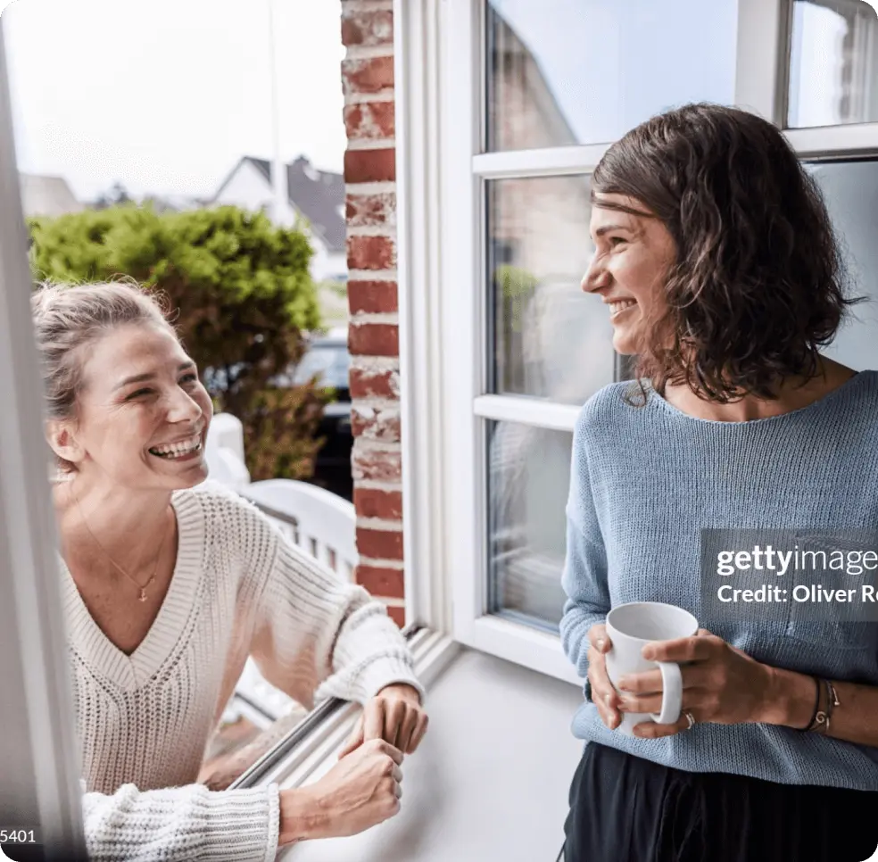 Two women laugh and have a conversation by a window