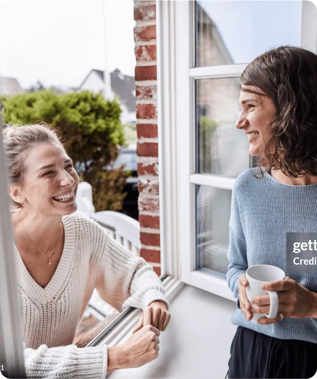 Two women laugh and have a conversation by a window